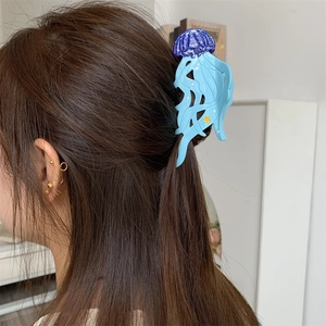 Détail d'une pince à cheveux méduse bleue et violette portée sur des cheveux bruns