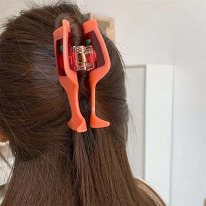 Detail showing an orange-pink acetate wine glass hair claw with cherry pattern on hair