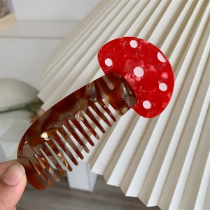 Dettaglio del pettine in acetato a forma di fungo rosso a pois con denti color ambra