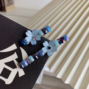 Détail de barrettes florales avec fleurs bleues mates et cristaux colorés sur base dorée