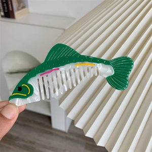 Dettaglio di un pettine creativo a forma di pesce in acetato verde e bianco perla