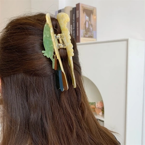 Detail view of colorful parrot-shaped acetate hair claw clip worn on model hair