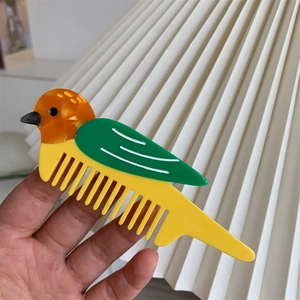 Dettaglio ravvicinato di un pettine in acetato a forma di uccello nei toni arancio e giallo