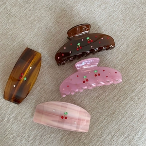 Detailed macro view of four acrylic hair clips with crystal cherry patterns and marble textures