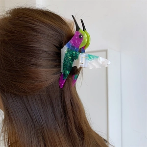 Detailed close-up of a colorful hummingbird acetate hair claw clip worn on long brown hair