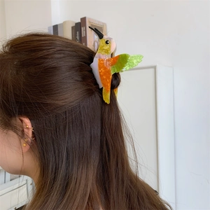 Detail of colorful hummingbird acetate hair claw clip styled on long dark hair
