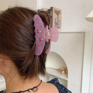Detail of purple translucent claw clip with cherry rhinestone design on model hair