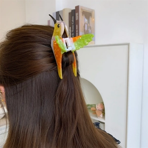 Detailed side view of a colorful acetate hummingbird hair claw clip worn on long brown hair
