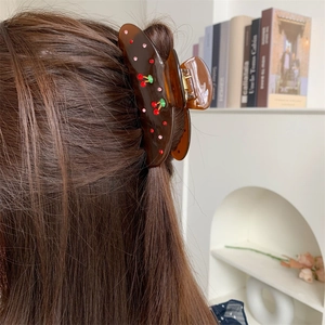 Detail view of amber brown translucent hair claw clip with cherry rhinestone decor on hair