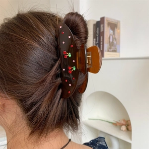 Macro detail of brown resin hair claw clip with red rhinestone cherry pattern on hair