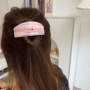 Pink marble texture hair claw with cherry design and rhinestones shown on brown hair