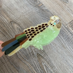 Detailed close-up of a colorful parrot-shaped acetate hair claw with vibrant feather patterns