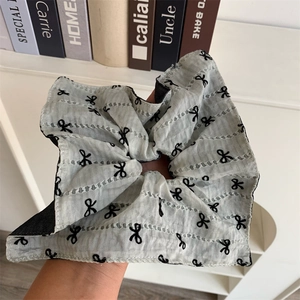Macro shot of oversized greyish-green pleated scrunchie with black bow pattern and cutout details