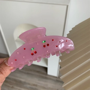 Detail showing pink translucent hair claw clip with red cherry rhinestone patterns