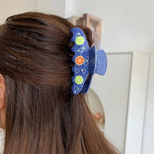 Dettaglio di una molletta per capelli in denim blu con motivi di limone e arancia
