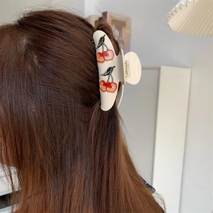 Detail showing red cherry pattern and sparkling rhinestones on the cream shark hair clip