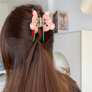 Détail de la pince à cheveux ours et pastèque en acétate portée pour une coiffure élégante