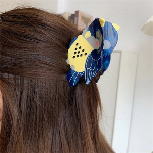 Detail of blue and yellow parrot hair claw clip made of high-quality acetate on dark hair