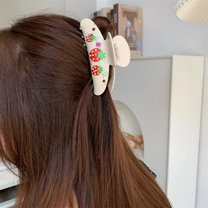 Close-up of a cream hair claw clip with red cherry rhinestones on a woman's hair