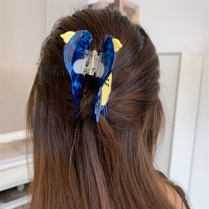 Detailed view of a blue bird-shaped acetate hair claw clip styled on long brown hair