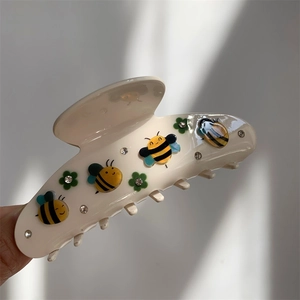 Dettaglio di un fermaglio per capelli bianco con piccole api, fiori verdi e strass lucidi