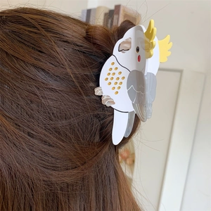Detail view of a white parrot-shaped acetate hair claw clip with golden polka dots