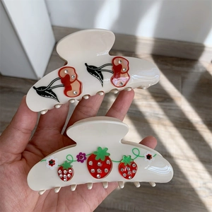 Close-up of cream acetate hair claw clips with sparkling cherry and strawberry rhinestones