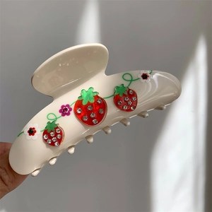 Macro view of cream shark hair clip featuring crystal-studded red strawberry motifs
