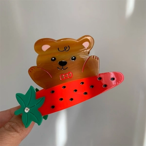 Détail d'une pince à cheveux en acétate avec un ours brun et une pastèque rouge