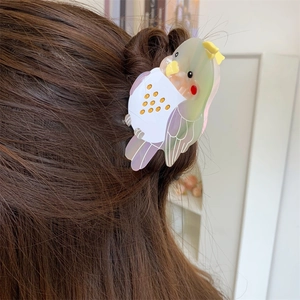 Detail of parrot-shaped acetate hair claw clip with pearlescent finish on dark hair
