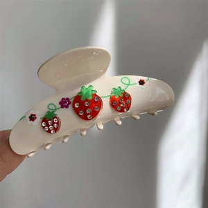 Close-up of cream white acetate hair claw with rhinestone cherry and floral motifs