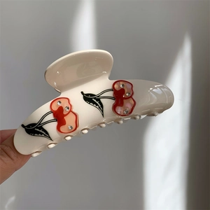 Detailed view of cream acetate hair claw clip featuring sparkling rhinestone cherry motifs