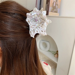 Close-up of shell-shaped white polka dot acetate hair claw clip worn on long brown hair