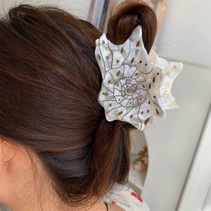 Detail of seashell hair claw with pearlescent acetate texture and gold spiral lines
