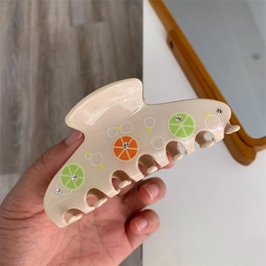 Dettaglio di una pinza per capelli beige con motivi a lime e strass scintillanti