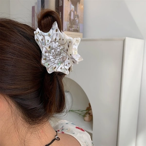 Macro detail of conch shell shaped hair claw clip with white pearl finish and spiral texture