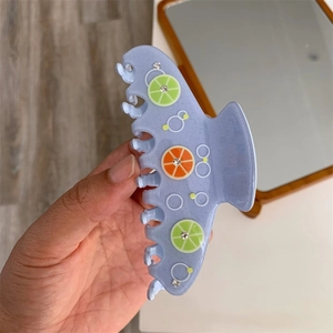 Dettaglio del fermaglio azzurro con motivi a lime e piccoli strass luminosi su superficie lucida
