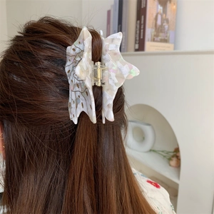 Detail of a pearlescent white acetate butterfly hair claw clip worn on a woman's bun hairstyle