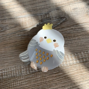 Detailed view of handmade cockatiel acetate hair claw clip on wooden background with sunlight
