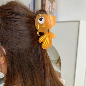 Vue détaillée d'une pince à cheveux en forme de poisson rouge sur cheveux bruns