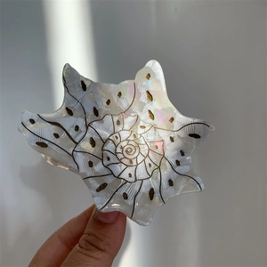 Macro detail of conch-shaped acetate hair claw with pearlescent finish and gold accents