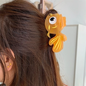 Détail d'une pince à cheveux en forme de poisson rouge orange portée sur une demi-queue
