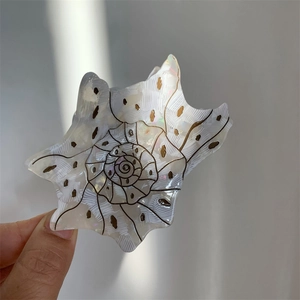 Elegant white shell hair claw with black texture and golden dots on a gray background
