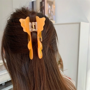 Pince à cheveux papillon orange en résine translucide sur de longs cheveux bruns
