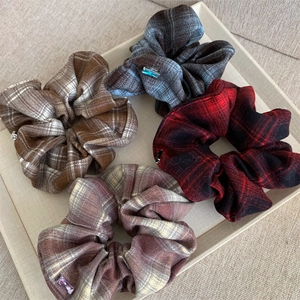 Close-up of four plaid scrunchies with crystal charms on a beige display tray