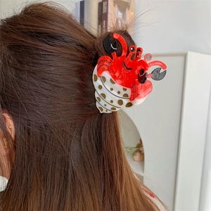 Pince à cheveux crabe et coquillage à pois présentée sur de longs cheveux bruns