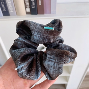 Retro plaid scrunchie with a blue gemstone detail in a hand-held close-up view
