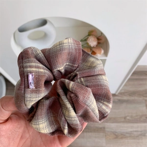 Detail view of a plaid scrunchie with a purple rhinestone held in hand for hair styling