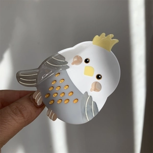 Detail of bird-shaped acetate hair claw featuring a cockatiel design with golden glitter