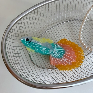 Dettaglio di un fermaglio per capelli a forma di pesce colorato in un cesto con perle